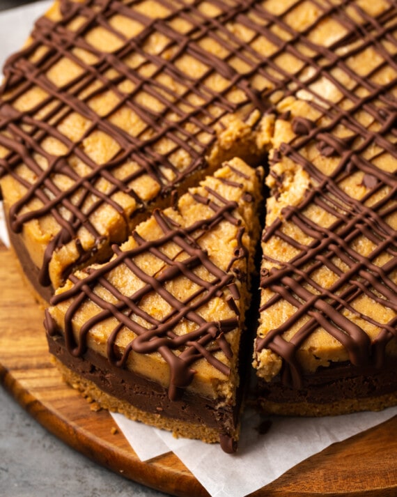 Reese's fudge pie topped with drizzles of chocolate sauce on a round wooden cutting board, with a slice cut out.