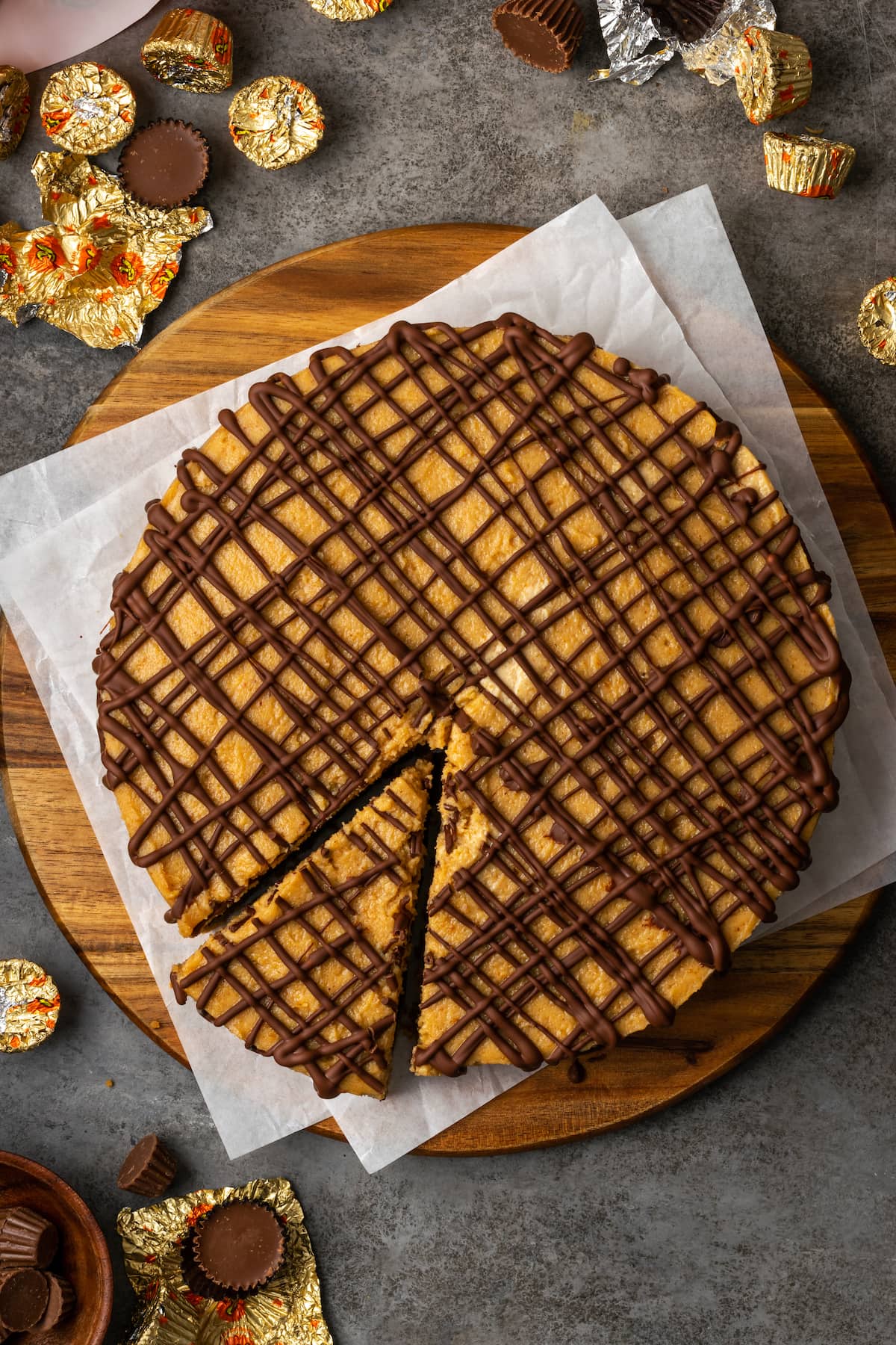 Overhead view of Reese's fudge pie topped with drizzles of chocolate sauce on a round wooden cutting board, with a slice cut out.