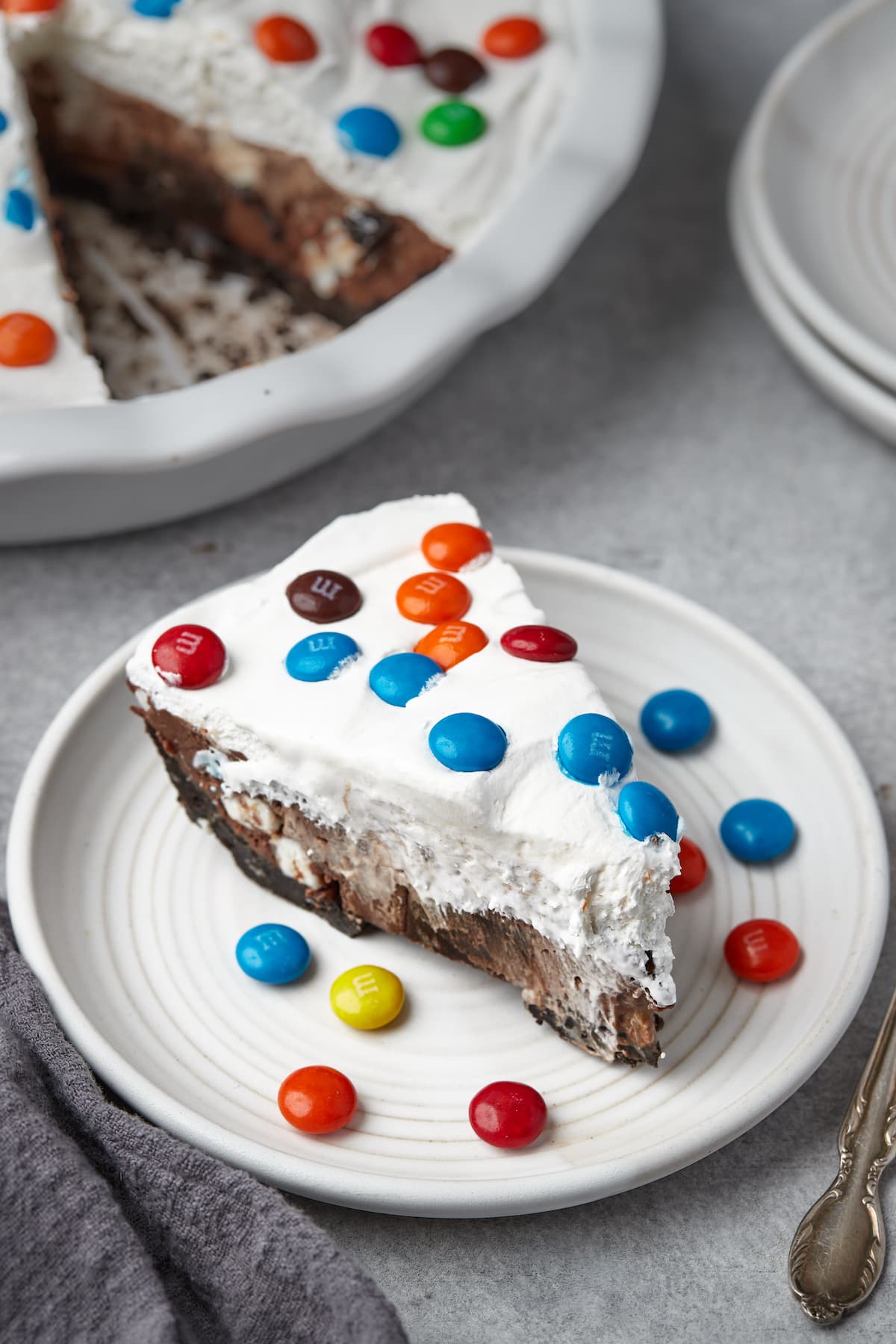 A slice of candy pie on a white plate, surrounded by scattered M&Ms.