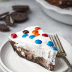 A slice of candy pie on a white plate, surrounded by scattered M&Ms.