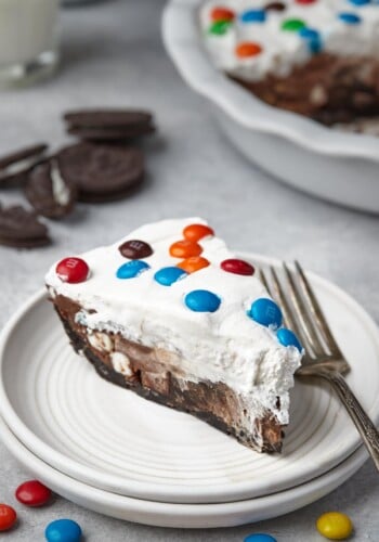 A slice of candy pie on a white plate, surrounded by scattered M&Ms.