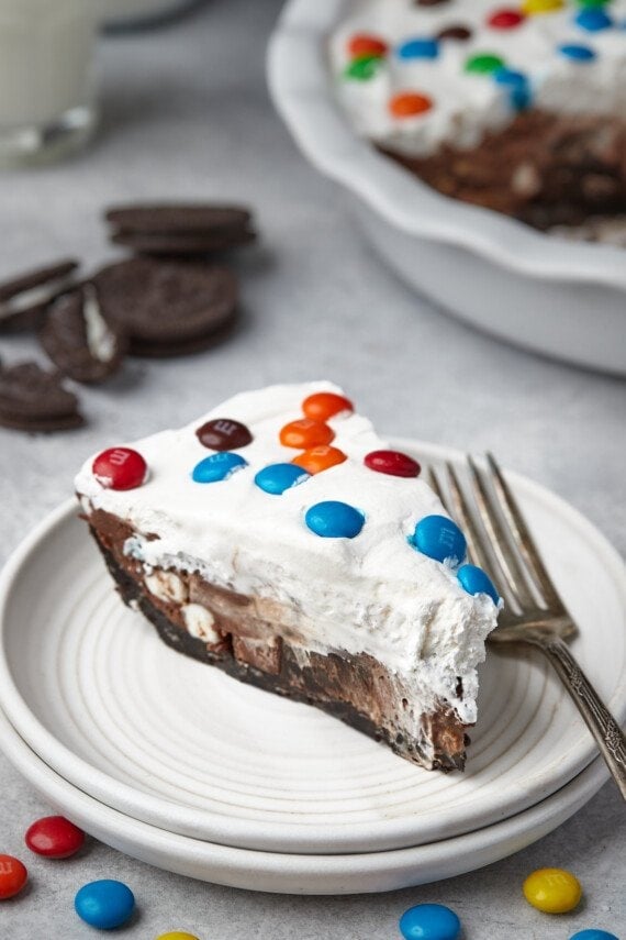 A slice of candy pie on a white plate, surrounded by scattered M&Ms.