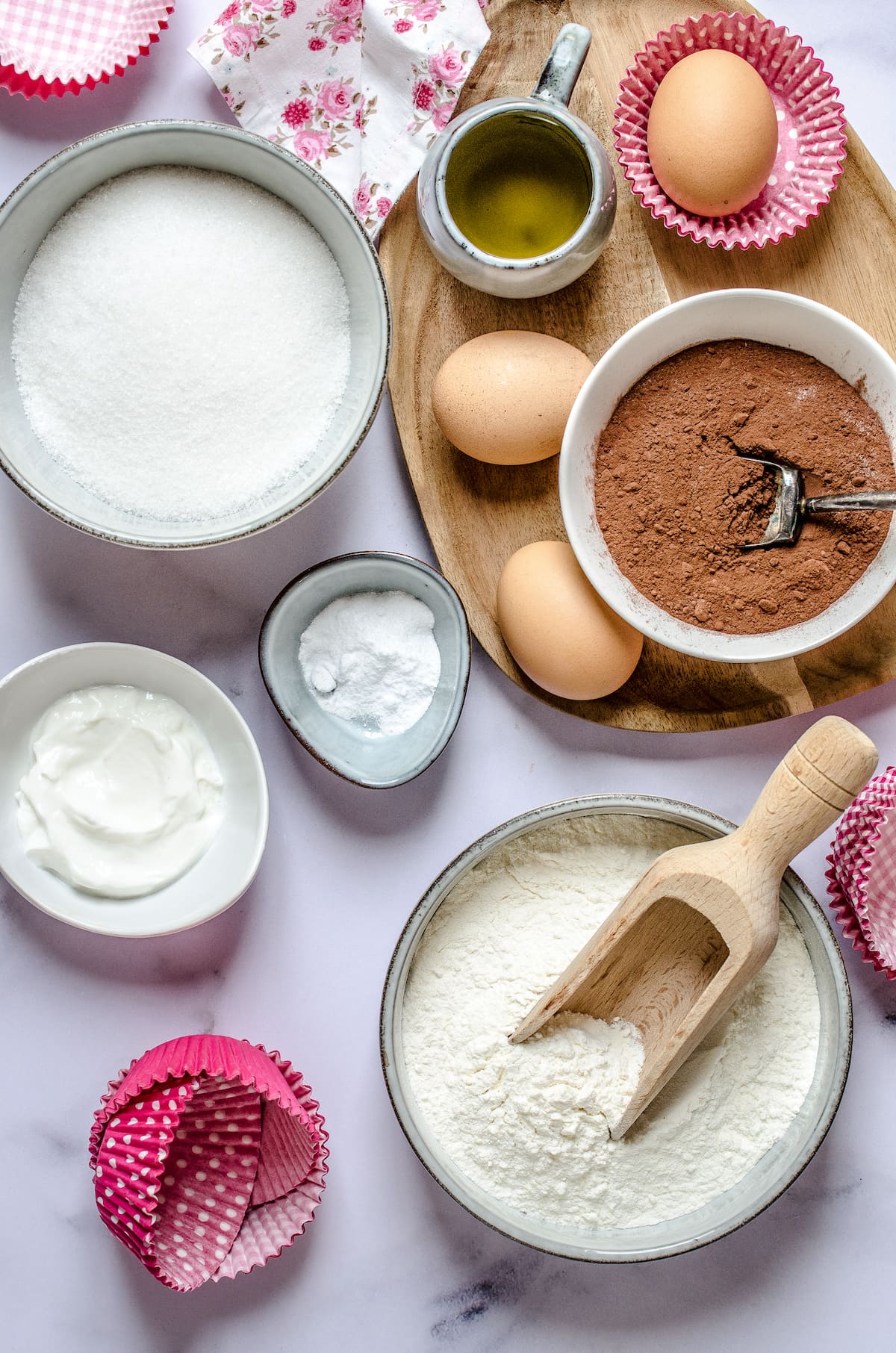 The ingredients for dark chocolate cupcakes: cocoa powder, milk, sugar, flour, eggs, vegetable oil, next to cupcake liners.