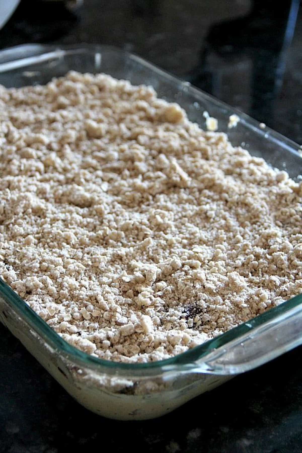 Unbaked peanut butter jelly bars topped with a crumble in a glass baking dish.