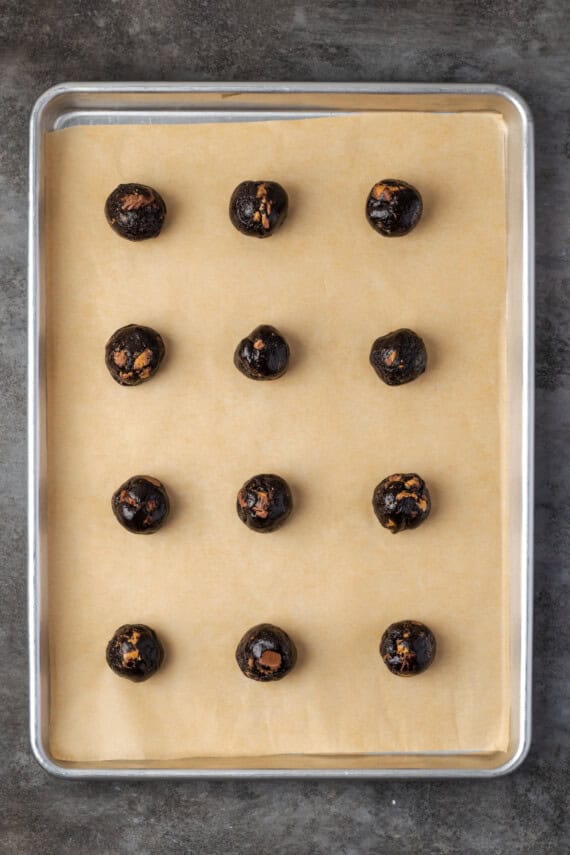 Rows of peanut butter chocolate cookie dough balls on a lined baking sheet.