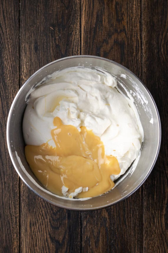 Sweetened condensed milk added to whipped cream in a mixing bowl.