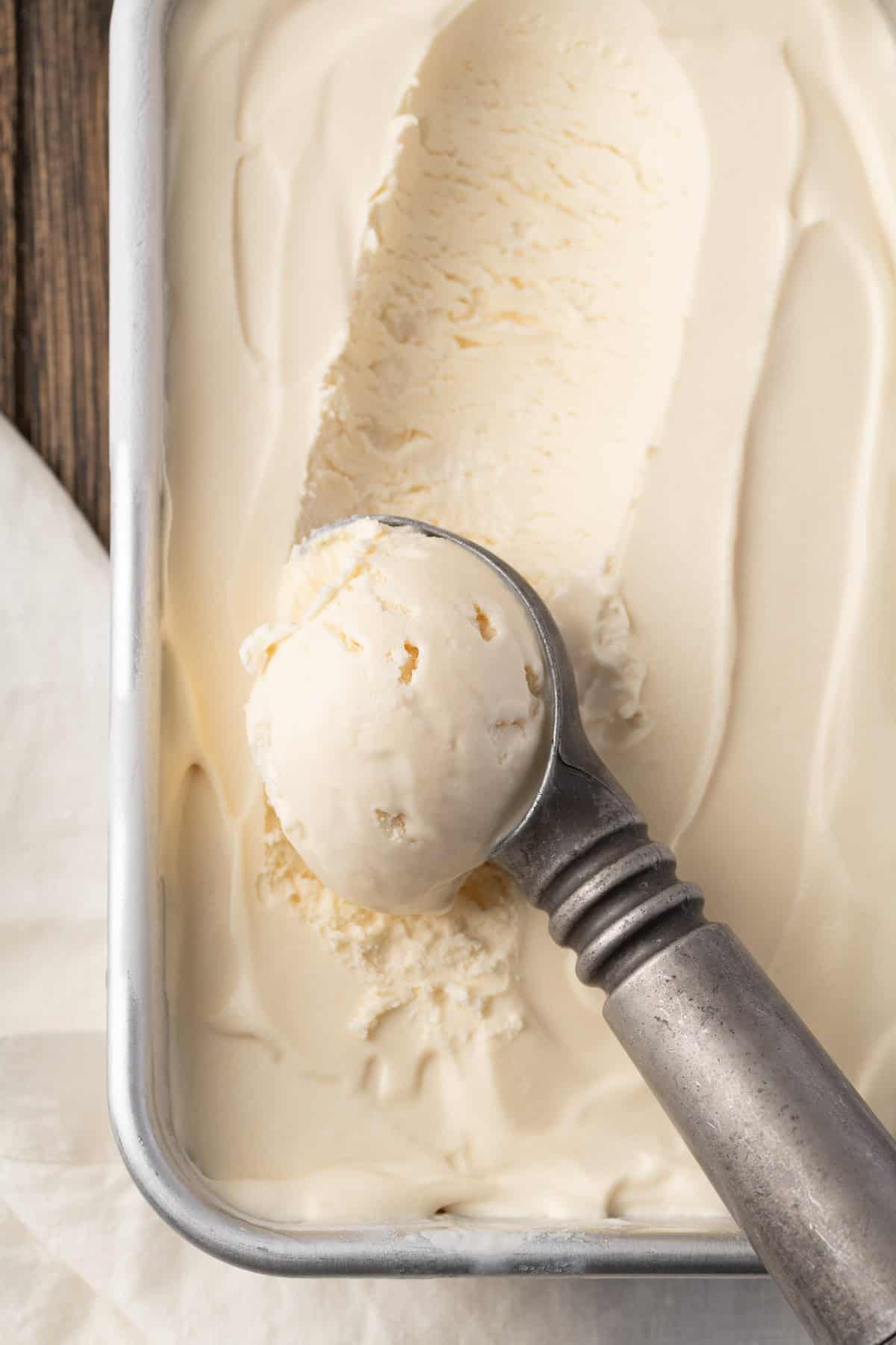 An ice cream scoop forming a scoop in a pan of vanilla ice cream.