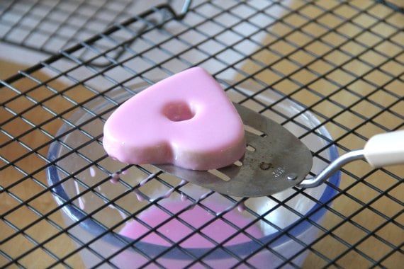 A pink-glazed Valentine's cookie on a wire rack.