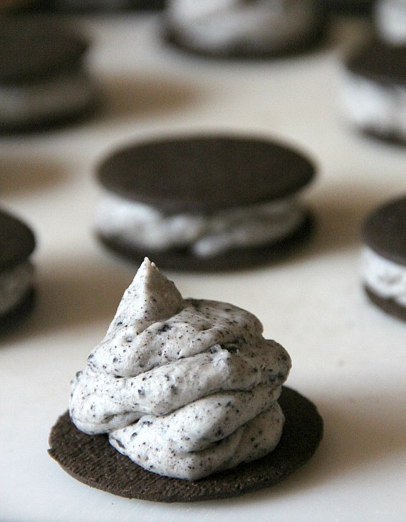A chocolate wafer cookie topped with a swirl of Oreo cheesecake frosting, with more sandwich cookies in the background.