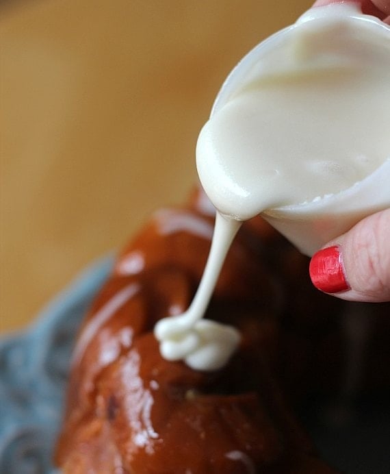 Vanilla icing being drizzled over baked cinnamon roll monkey bread.