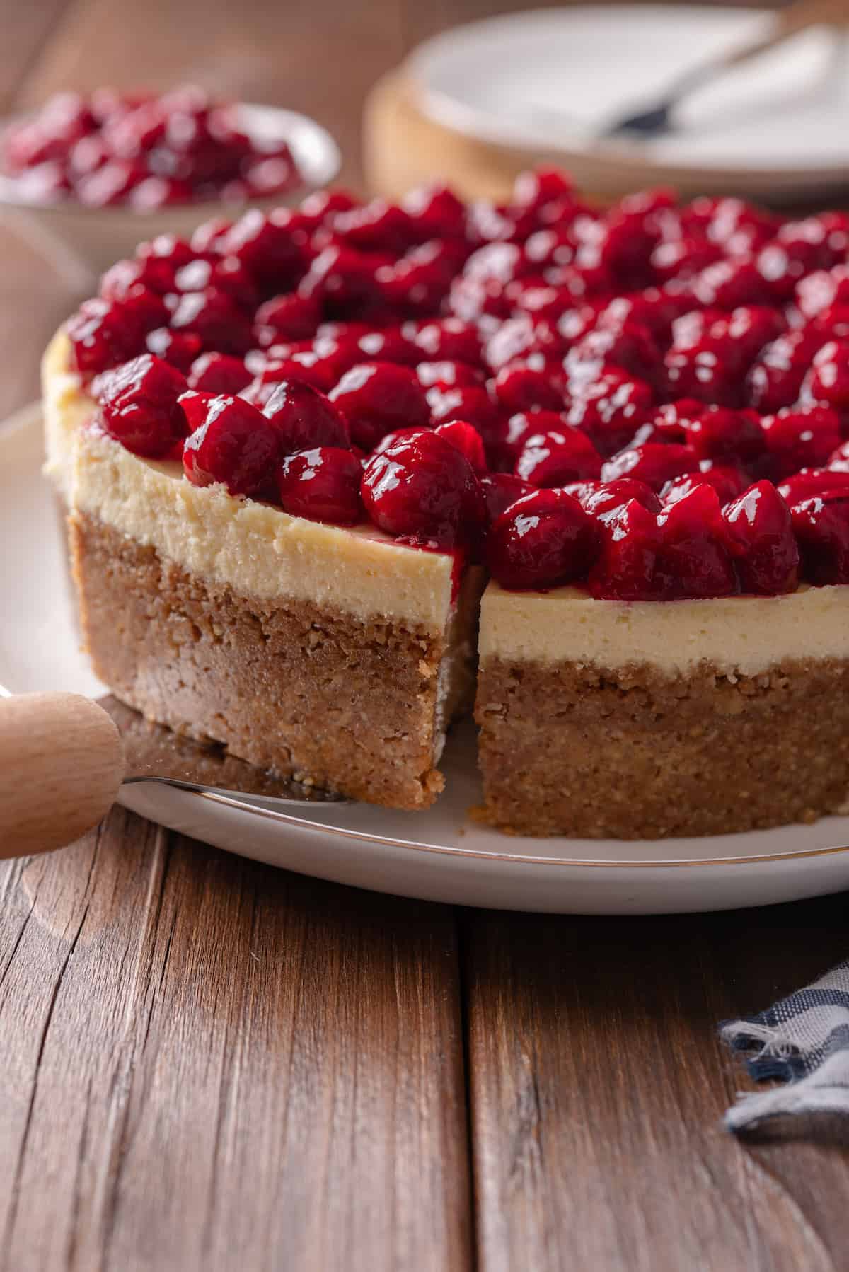 A cake server sliding underneath a slice of cherry cheesecake cut from the rest of the cheesecake on a plate.