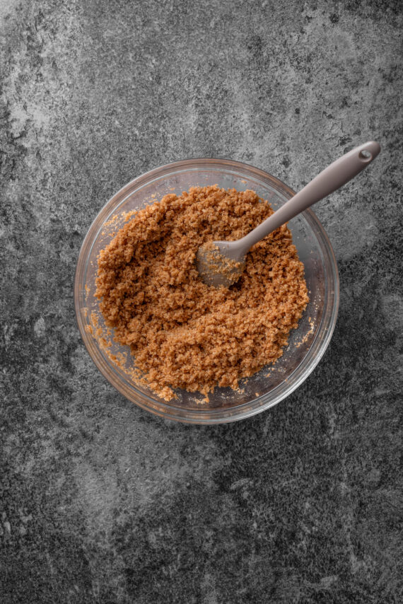 Graham cracker crust mixture in a glass bowl with a spoon.