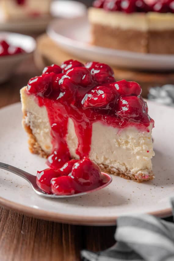 A spoonful of cherry pie filling next to a slice of cherry cheesecake on a plate.