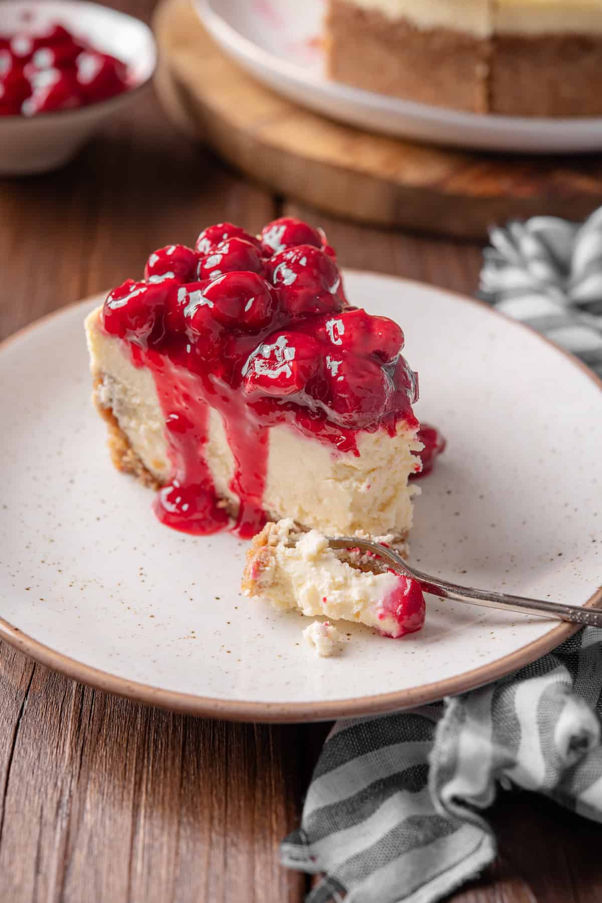 A slice of cherry cheesecake on a white plate with a forkful missing from the end.