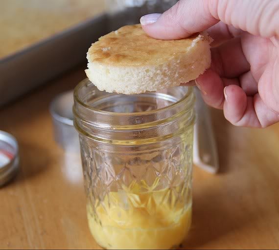 A circle of vanilla cake being put on top of vanilla pudding in a jar