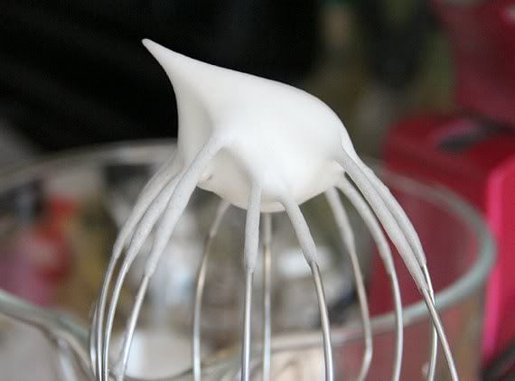 Egg whites forming soft peaks on the whisk of a stand mixer