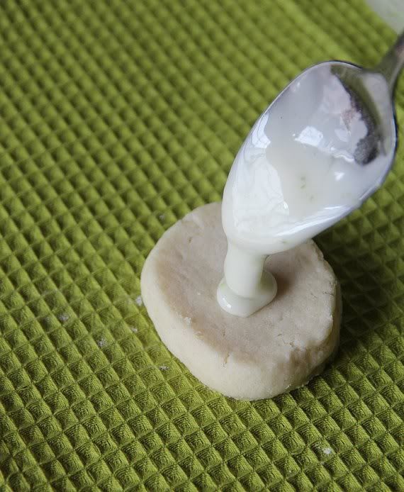 Lime glaze being spooned onto a round shortbread cookie