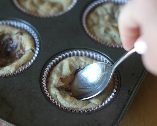 Baked cookie cups in a muffin tin with a spoon pressing into the middle of one cookie cup