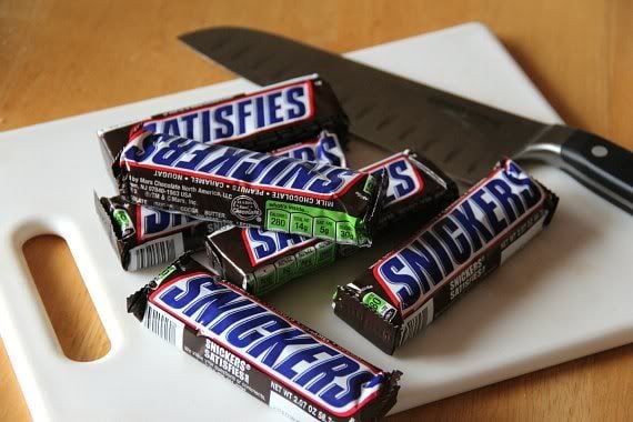 Wrapped Snickers bars on a cutting board with a knife
