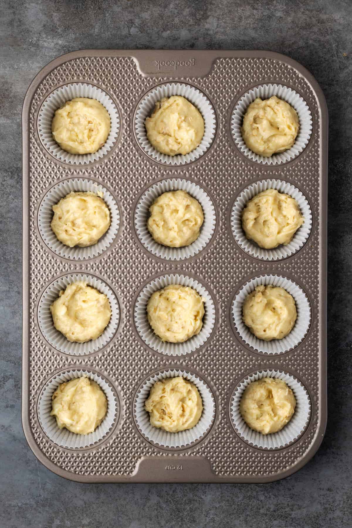 Cinnamon muffin batter in a lined 12-well muffin pan.