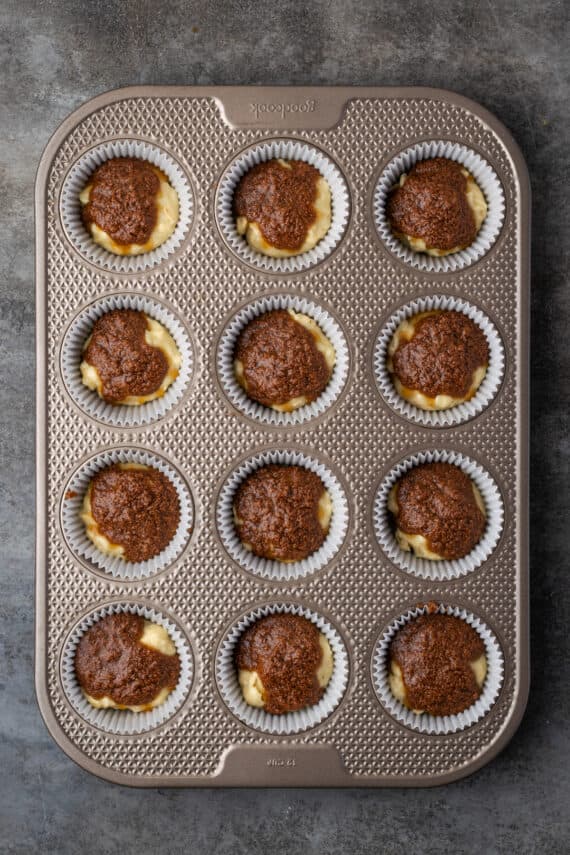 Cinnamon muffin batter topped with cinnamon sugar filling in a 12-well muffin pan.