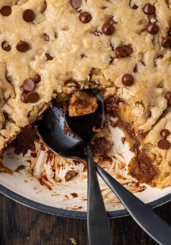 Overhead view of a skillet chocolate chip cookie with a serving missing and a spoon resting in the open space.