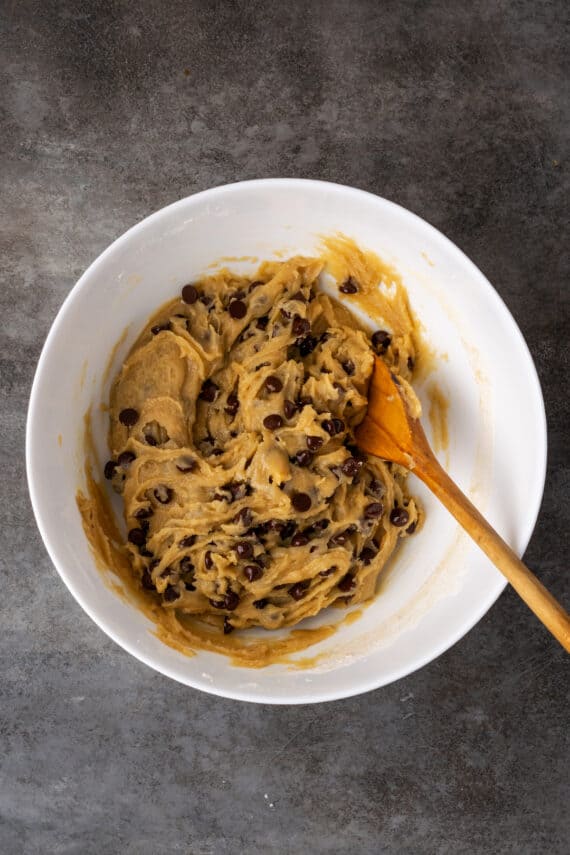 Chocolate chip cookie dough in a white bowl with a wooden spoon.