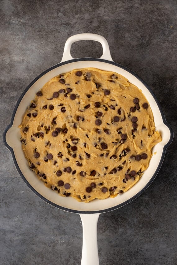 Chocolate chip cookie dough spread into a large cast iron skillet.