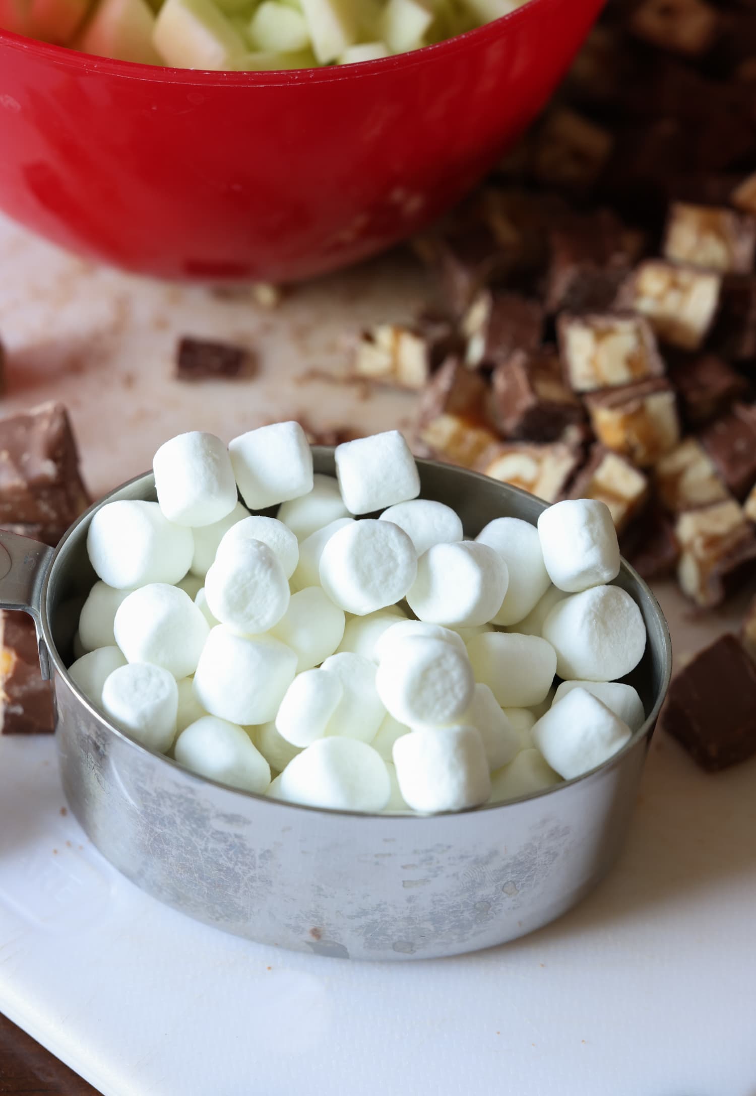 Mini marshmallows in a measuring cup and Snickers bars carved on a cutting board