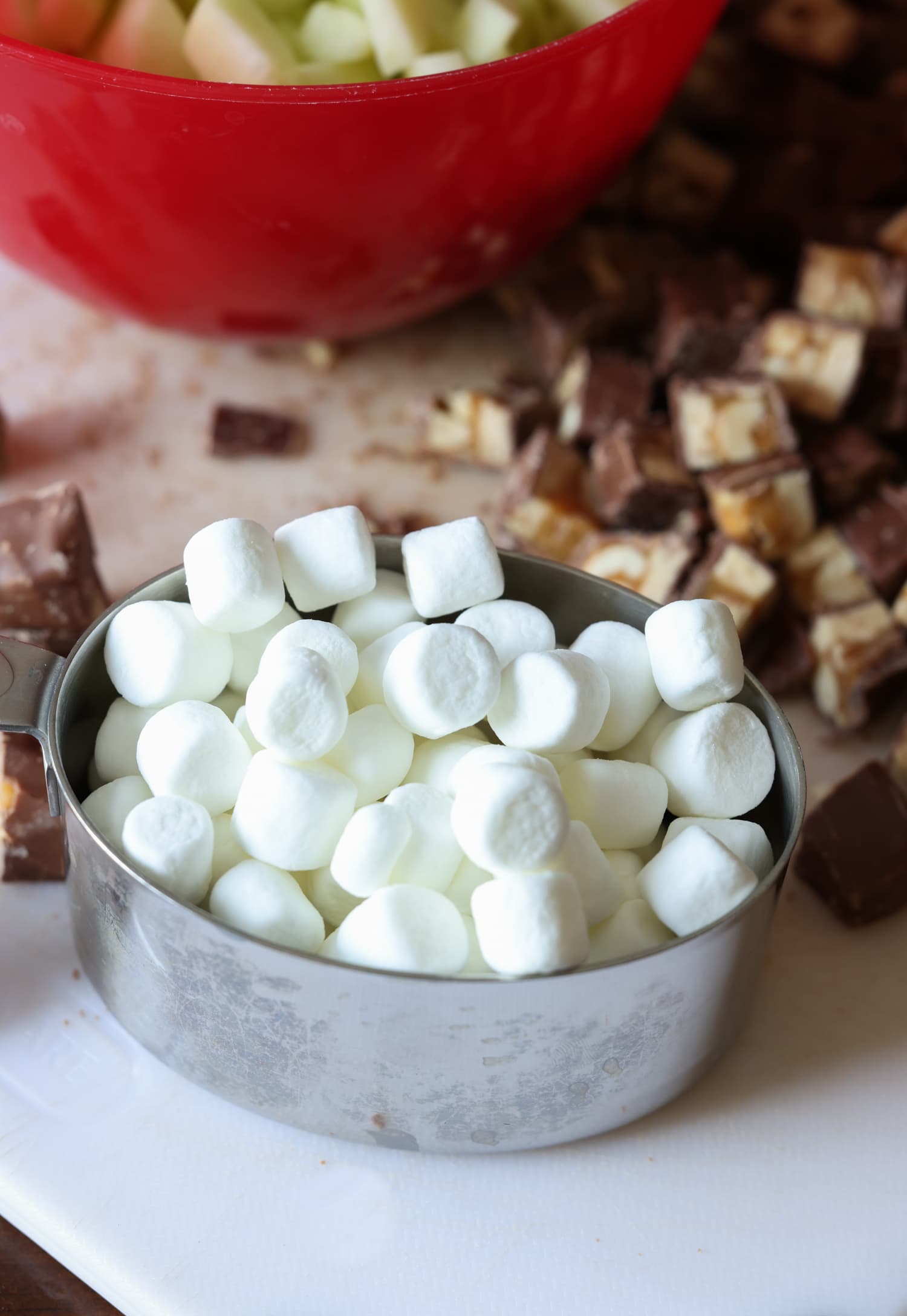 Mini-Marshmallows in einem Messbecher mit gehackten Snickers-Riegeln auf einem Schneidebrett