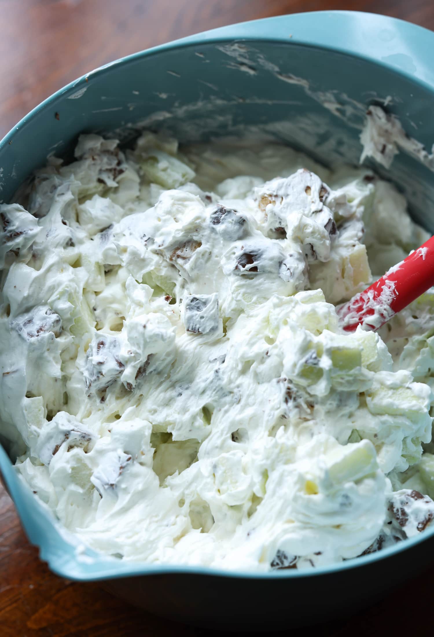Place cream cheese, cool whip, chopped Snickers, chopped apple, and mini marshmallows into a mixing bowl using a red rubber spatula.
