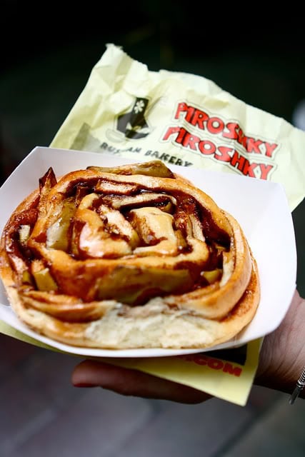 A cinnamon roll pastry on a plate with a Piroshky Piroshky bag