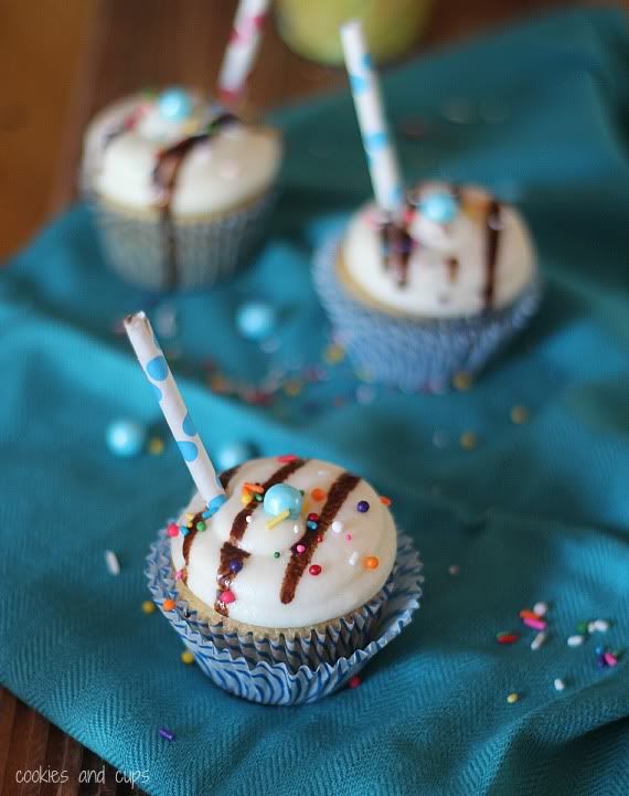 Root beer float cupcakes decorated with chocolate drizzle, sprinkles, and a straw coming out the top