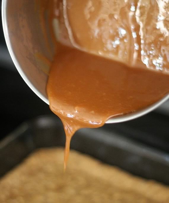 Melted caramel being poured over cookie base in a 9x13 pan
