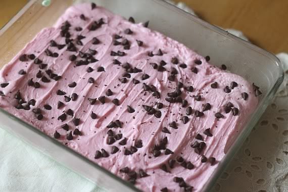 Mini chocolate chips on top of pink and green layered fudge in a pan