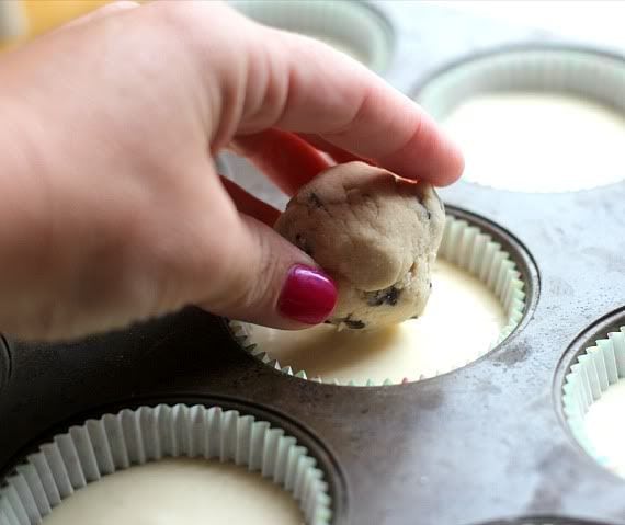 A cookie dough ball being placed in batter in a muffin tin