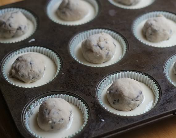A muffin tin filled with batter and a ball of cookie dough in each cup