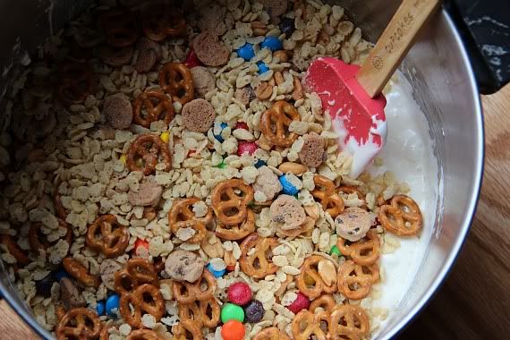 Melted marshmallow being stirred into dry ingredients for trail mix krispie treats