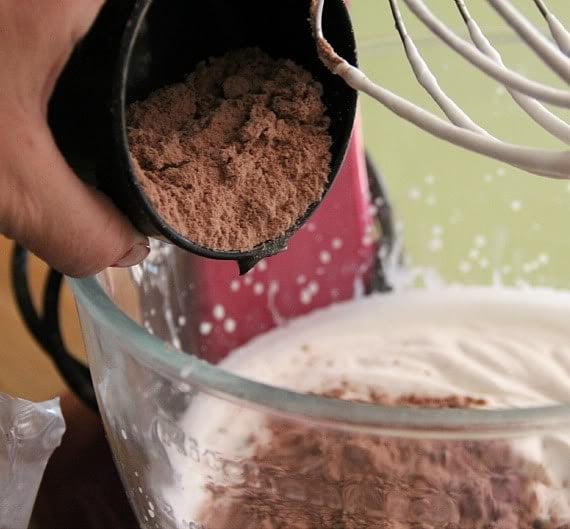 Dry brownie mix being added to a mixing bowl of whipped cream