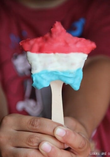A hand holding a red white and blue star shaped krispie treat on a stick