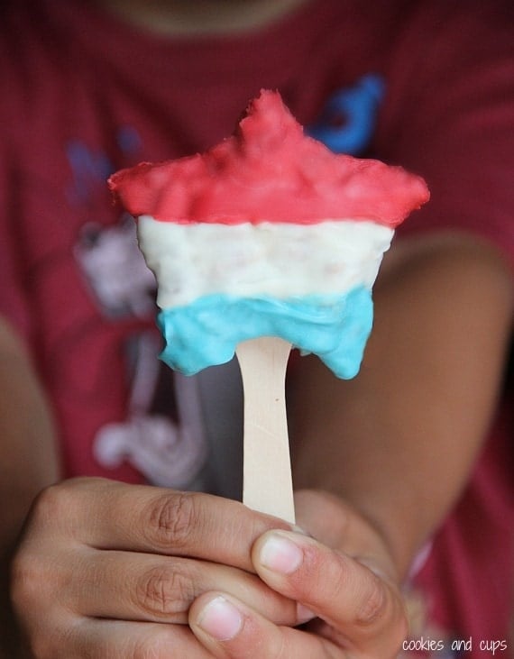 A hand holding a red white and blue star shaped krispie treat on a stick
