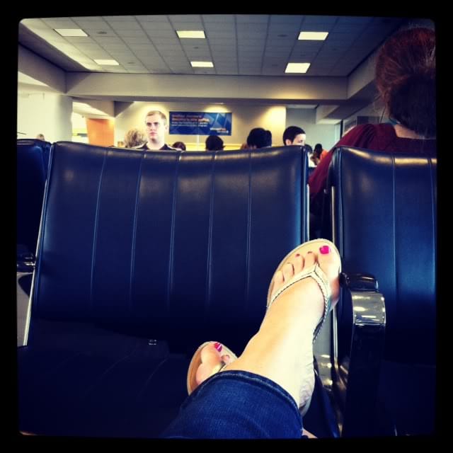 A woman's feet resting on a set of chairs at the airport