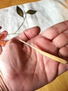 A hand-whittled toothpick in the palm of a hand