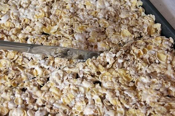 A jelly roll pan of cereal and marshmallow mixture being cut in half