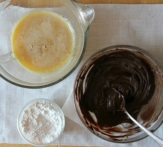 Top view of bowls of chocolate batter, melted butter, and flour