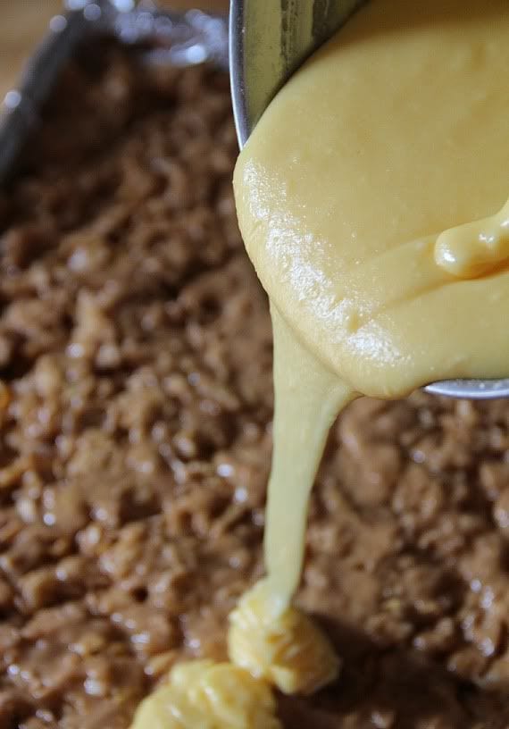 Vanilla pudding mixture being poured over a pan of peanut butter crunch mixture