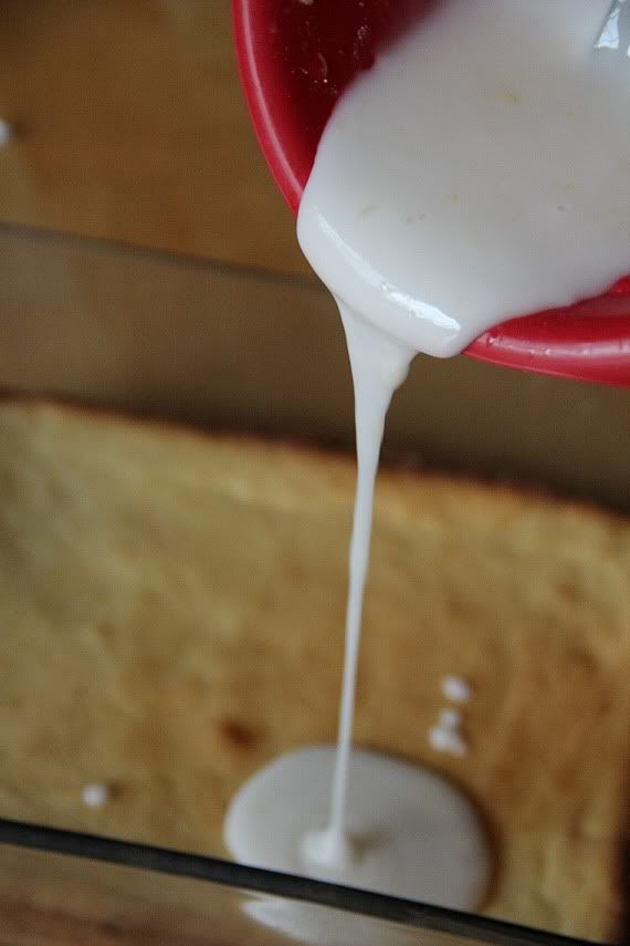 Lemonade glaze being poured over baked lemon brownies in the pan.