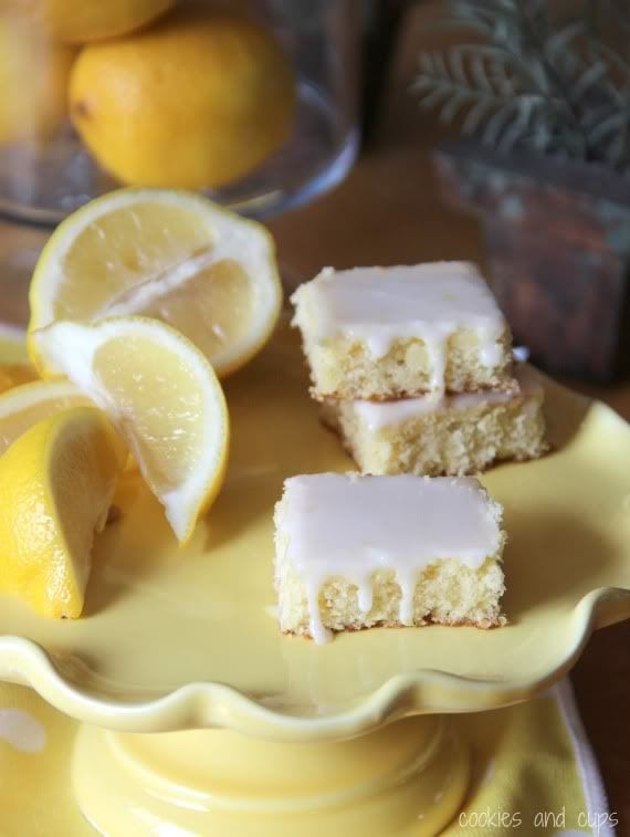 Three lemon brownies next to lemon wedges on a yellow plate.