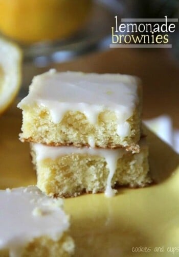 Two lemon brownies stacked on a yellow plate with a text overlay that reads "Lemonade Brownies".