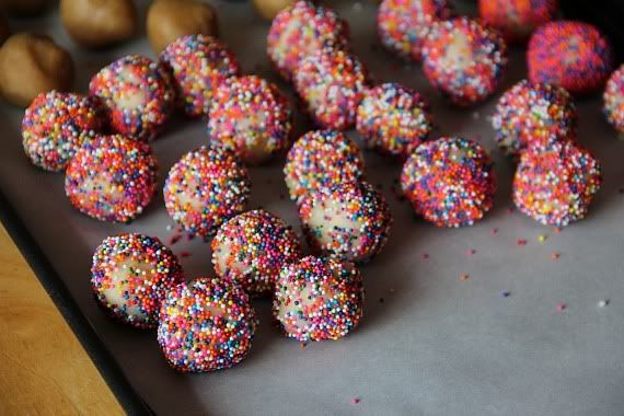Cookie dough balls coated in rainbow sprinkles on a parchment-lined baking sheet